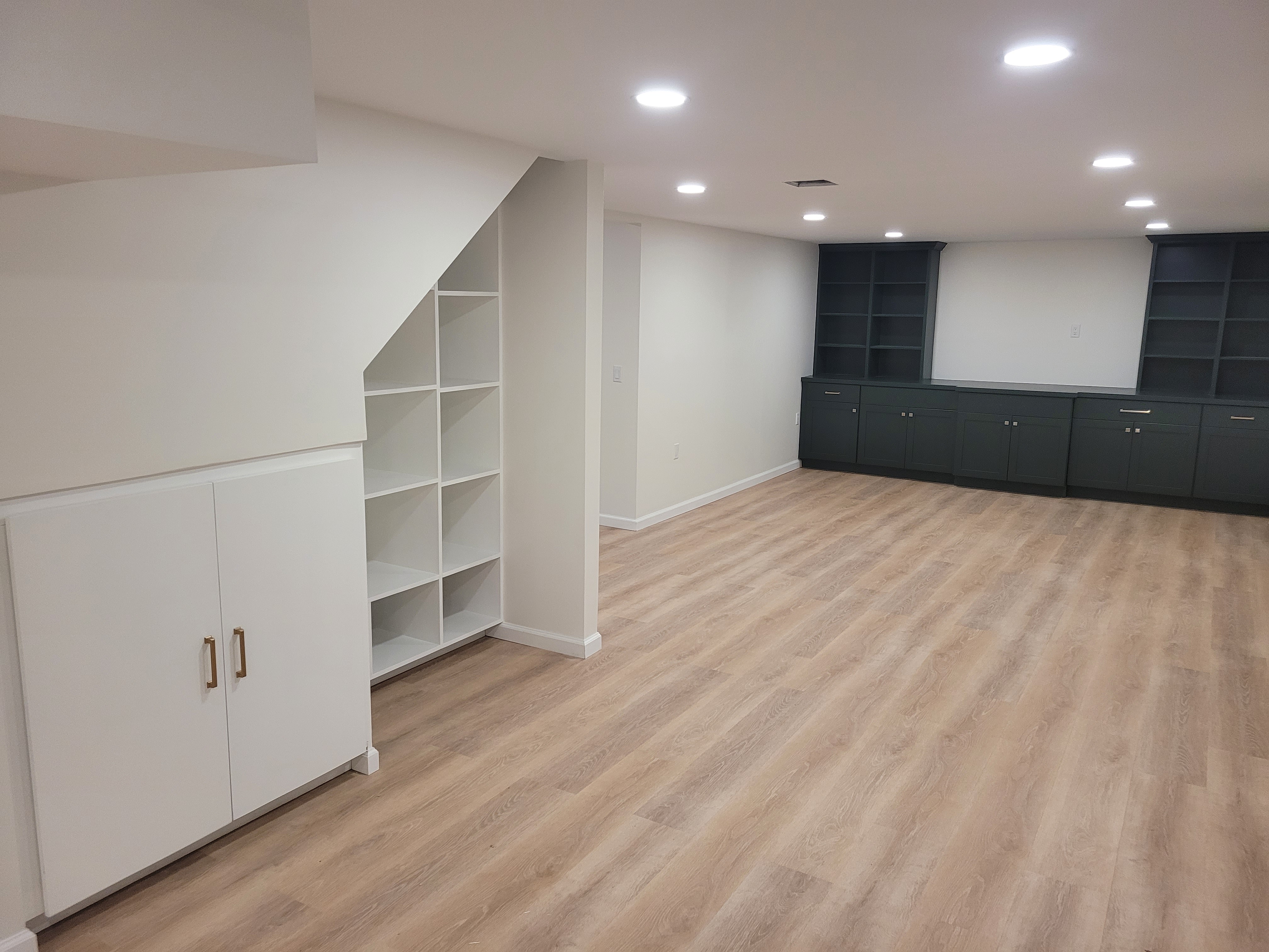 Finished basement with white built-in shelving tucked under the stairs beside a dark accent wall by Rome Leite Home Improvement in Danbury, CT
