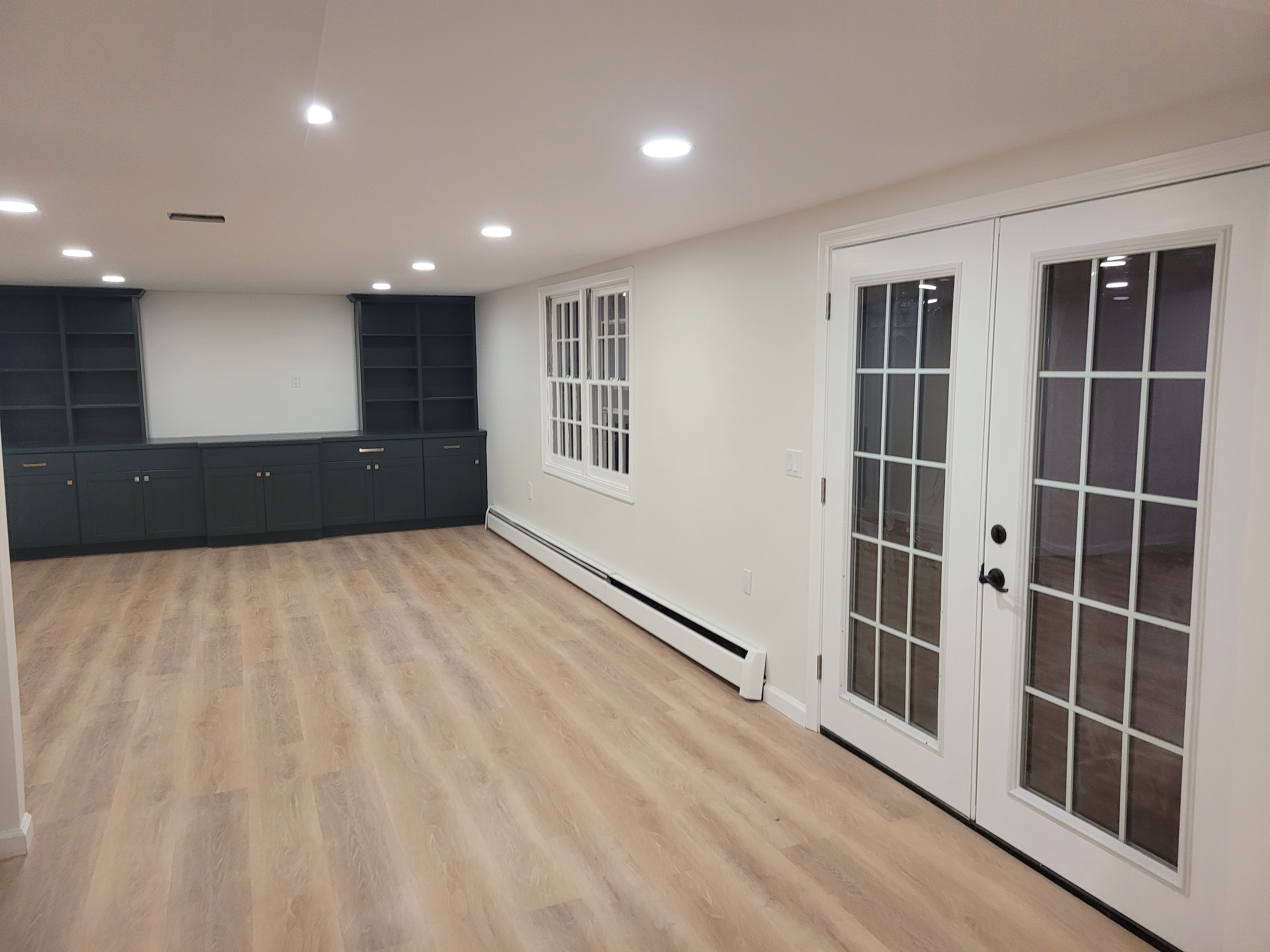 Finished basement with French doors and a window, dark built-in cabinetry in the background by Rome Leite Home Improvement in Danbury, CT
