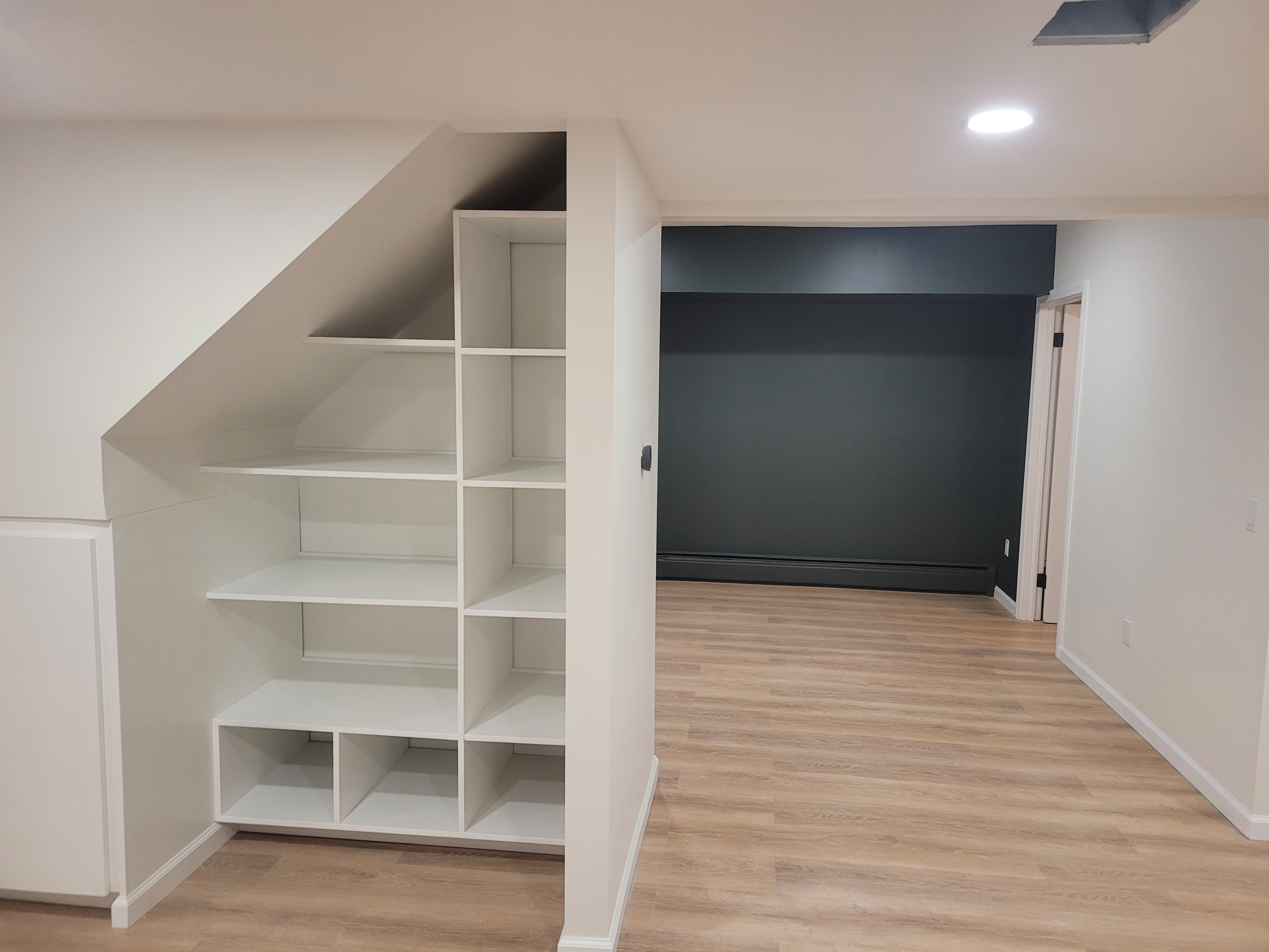Finished basement understair storage nook with white built-in shelving next to a dark accent wall by Rome Leite Home Improvement in Danbury, CT