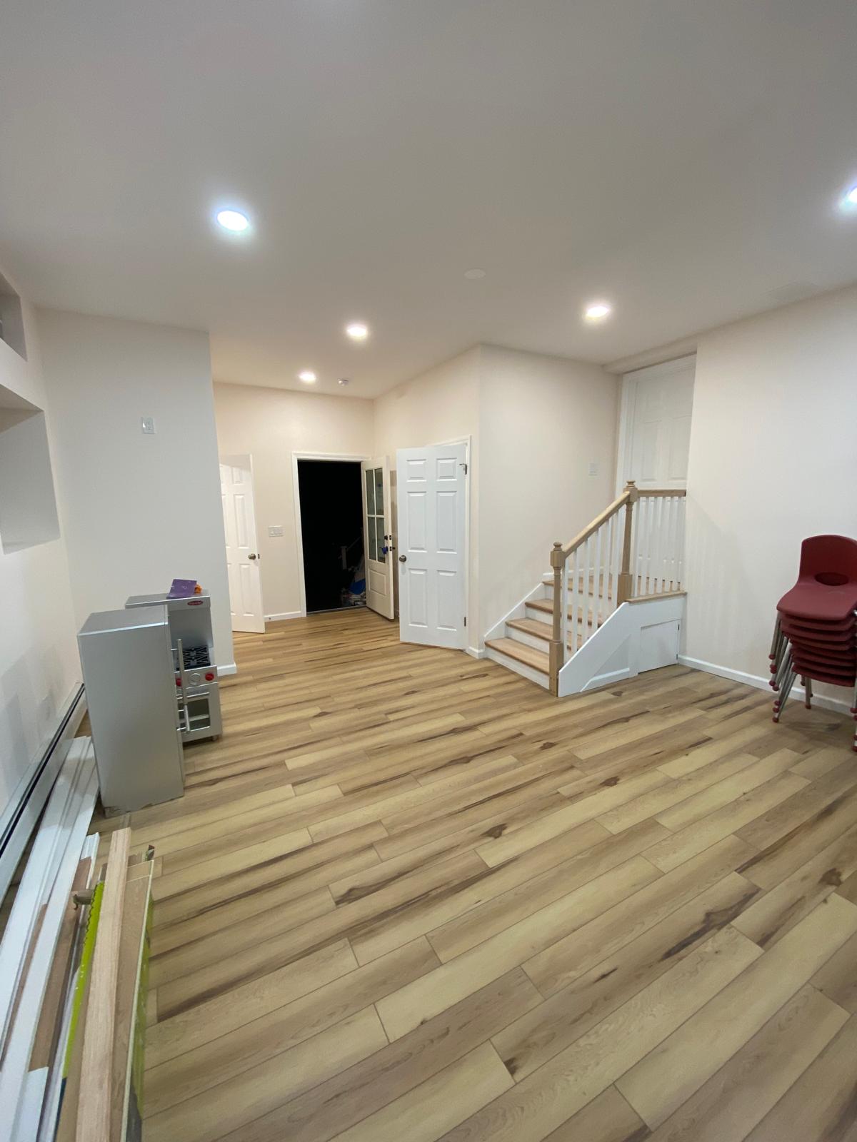 Basement hallway with white doors, a staircase with railing, and a small storage cabinet unit by Rome Leite Home Improvement in Danbury, CT