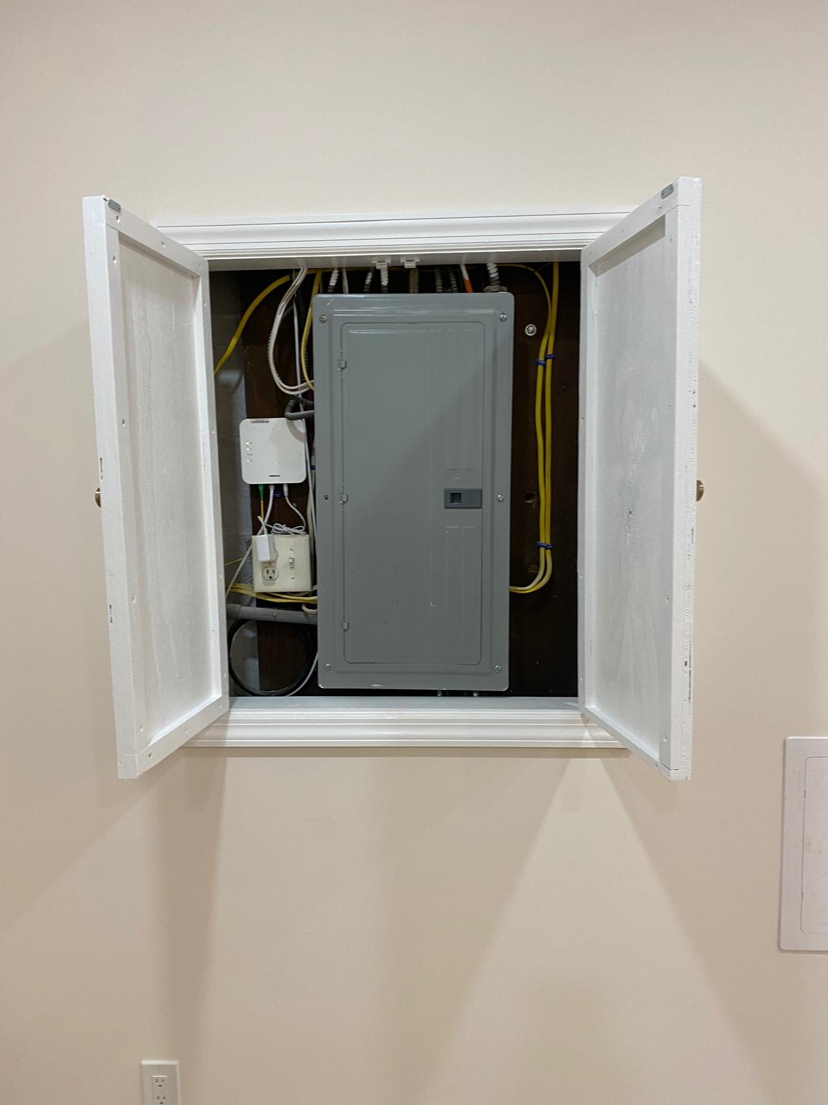 Open wall access panel in a basement revealing an electrical panel and wiring by Rome Leite Home Improvement in Danbury, CT