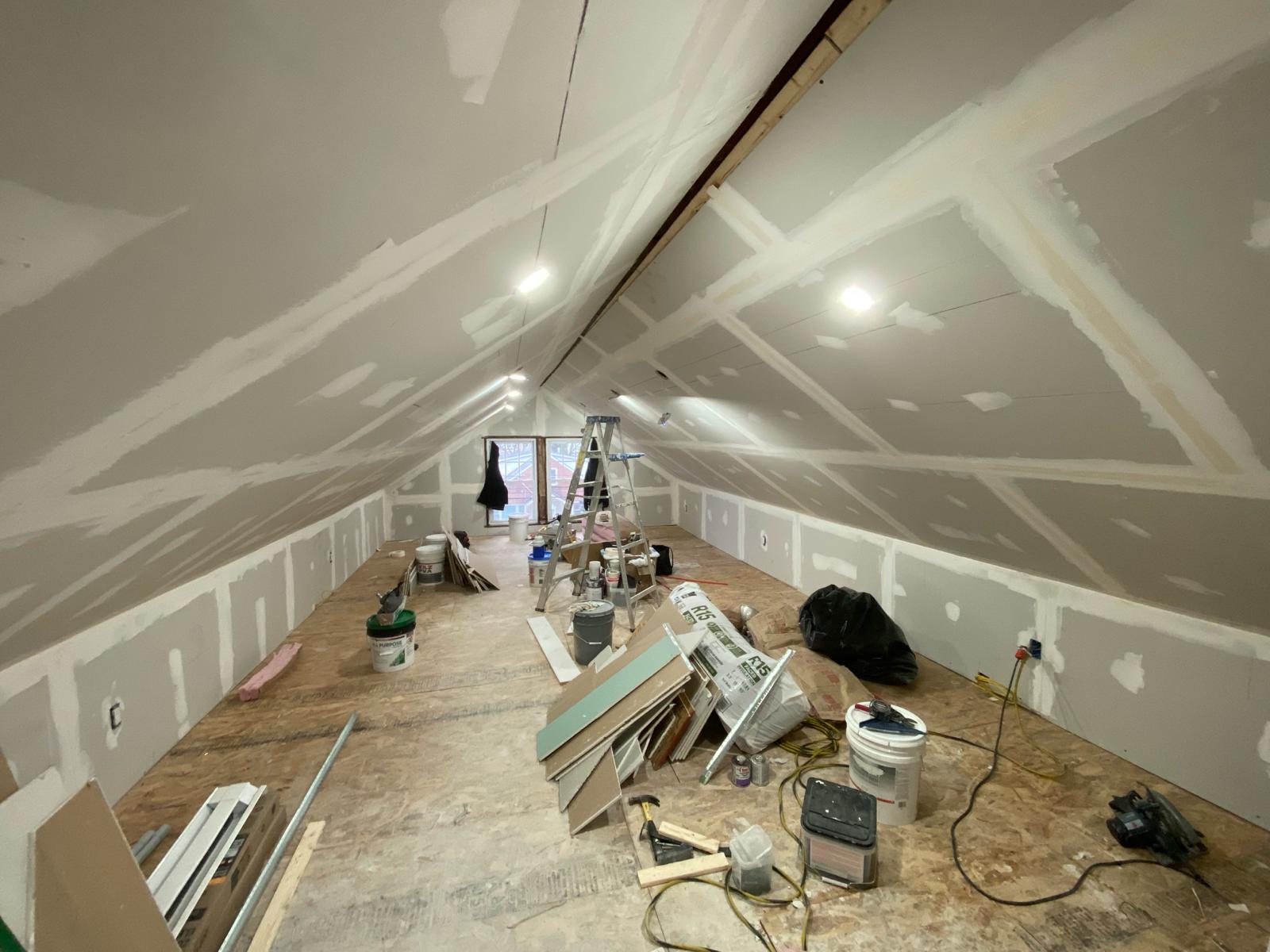 Attic room mid-renovation with taped drywall on the sloped ceiling and a ladder by Rome Leite Home Improvement in Danbury, CT