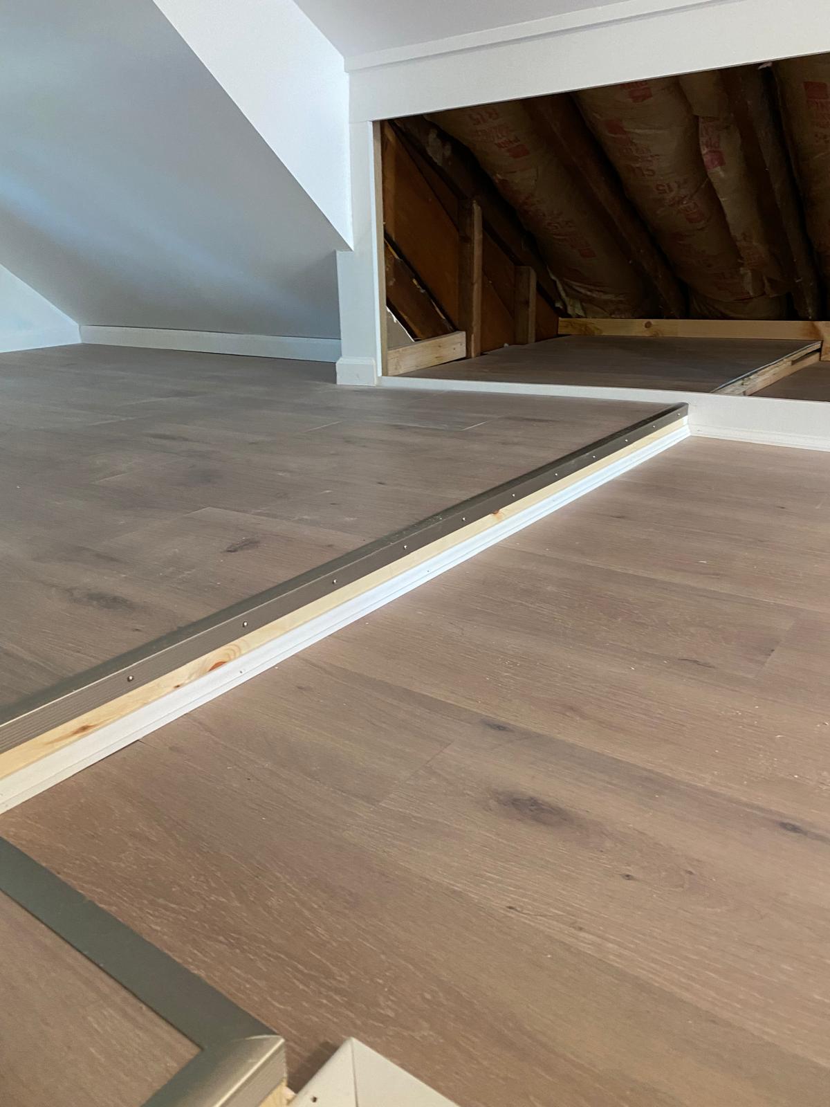 Newly installed hardwood flooring next to an unfinished attic storage area with exposed insulation by Rome Leite Home Improvement in Danbury, CT