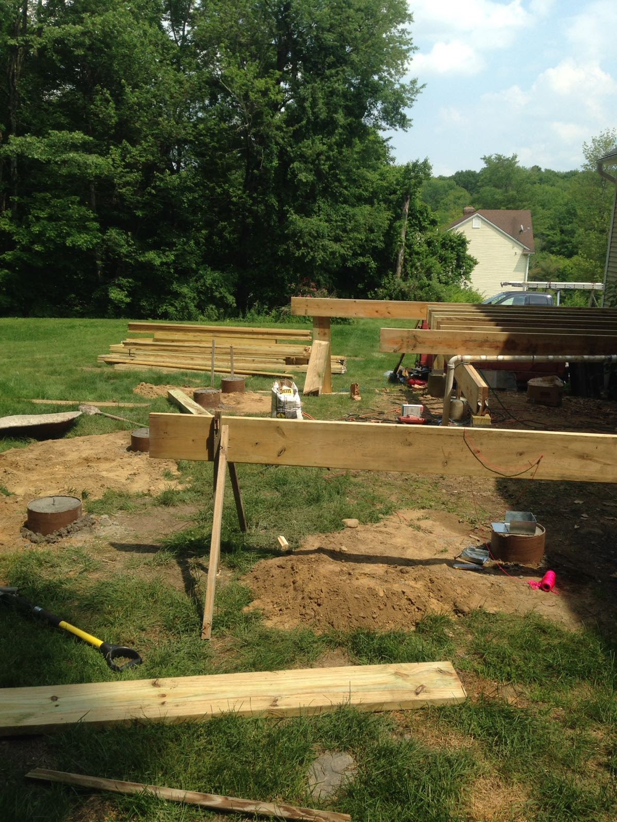 Backyard deck framing under construction with stacked lumber and concrete footings by Rome Leite Home Improvement in Danbury, CT