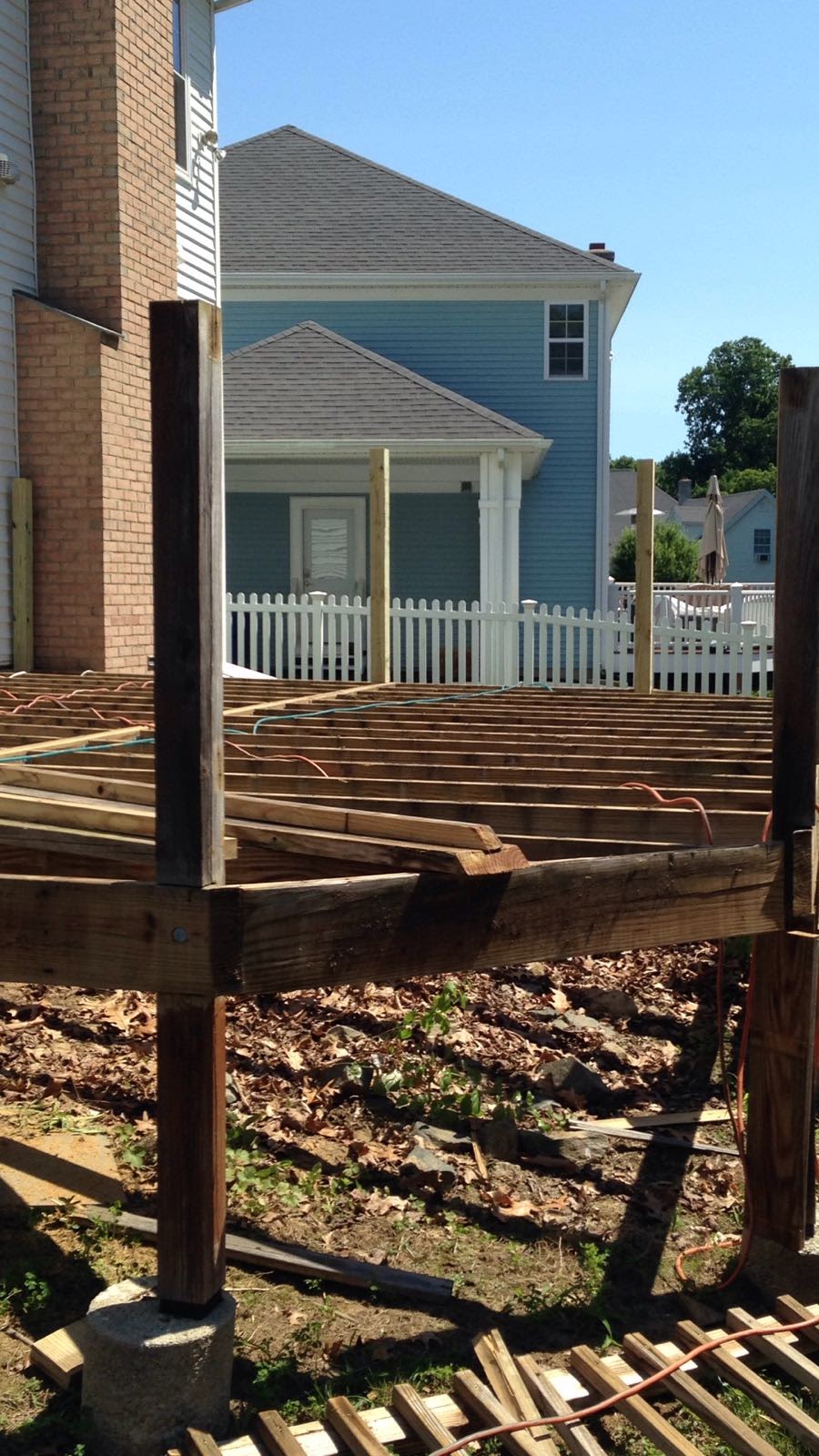 Corner post of a deck under construction with joists and a white picket fence by Rome Leite Home Improvement in Danbury, CT