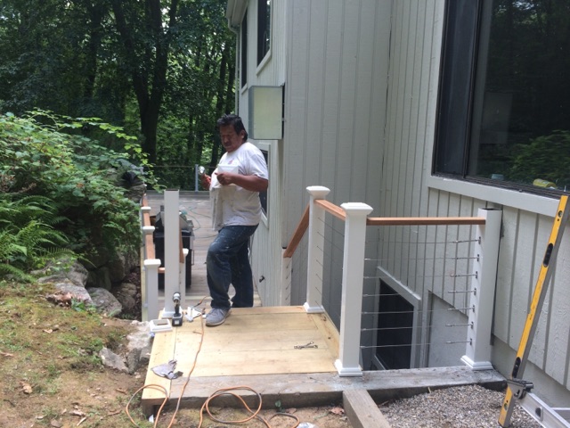 A worker standing on a newly built wood deck with white posts and cable railing by Rome Leite Home Improvement in Danbury, CT