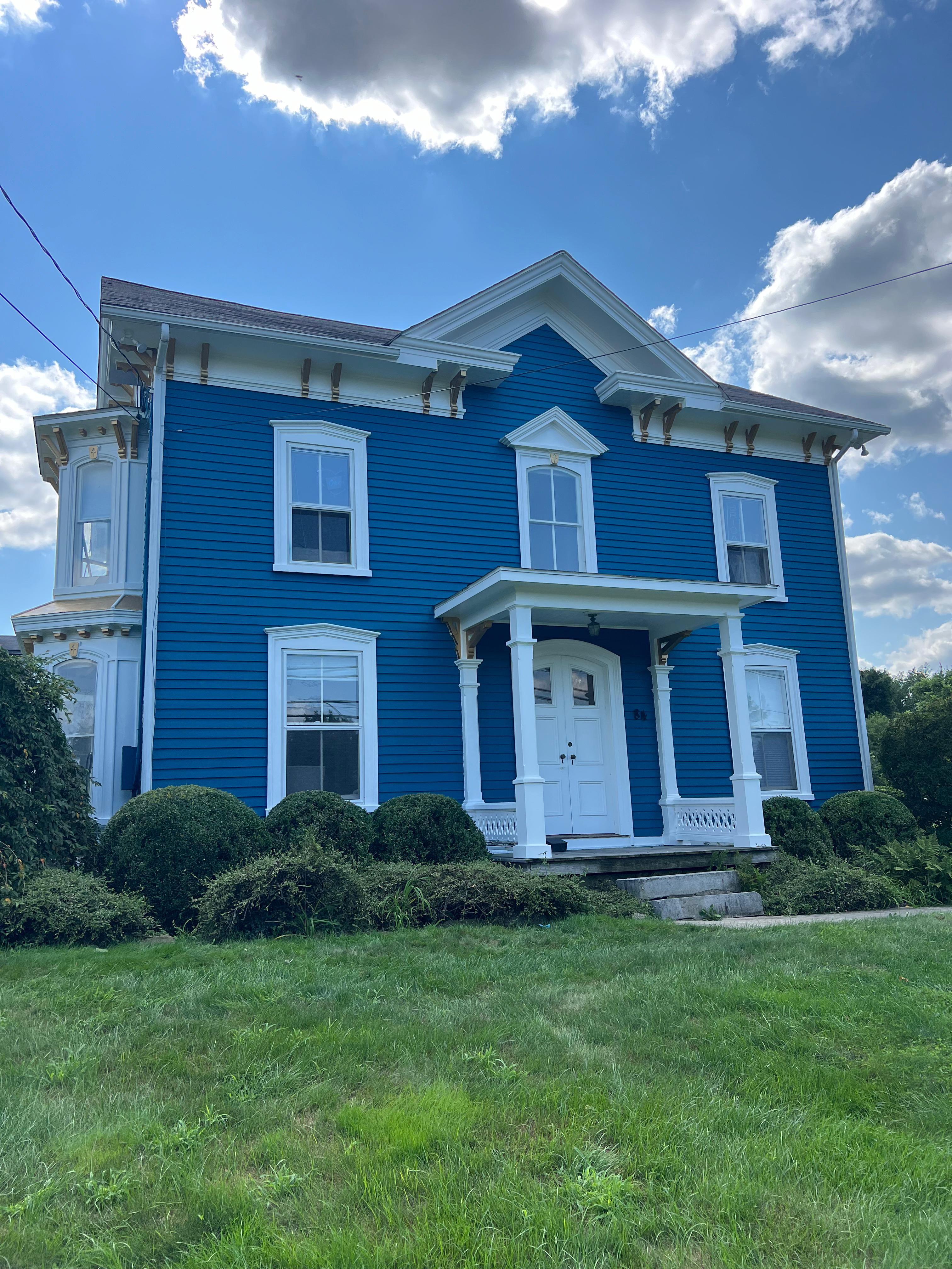 Front elevation of a freshly painted blue Victorian house with white trim and a covered porch by Rome Leite Home Improvement in Danbury, CT