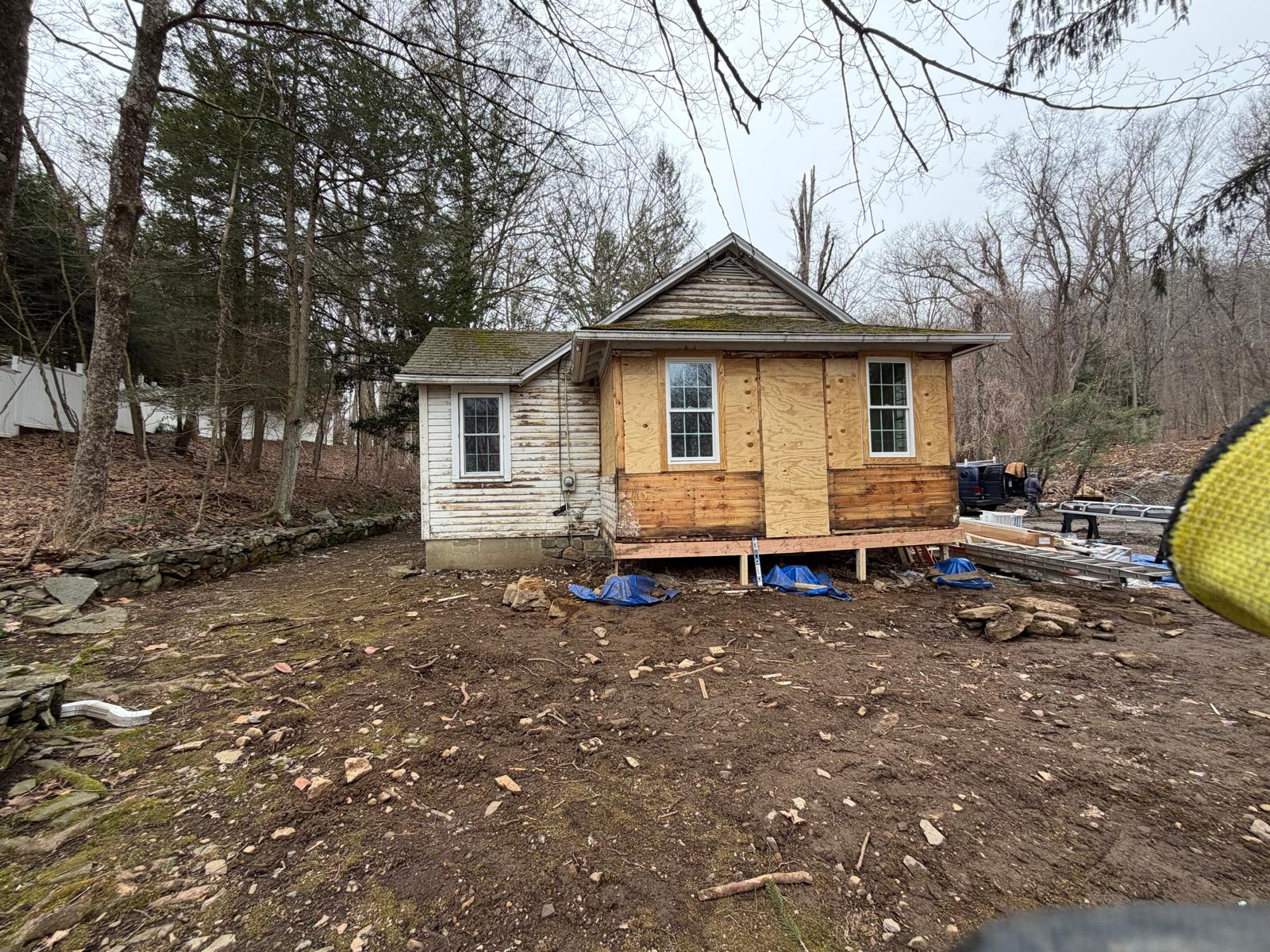 Side exterior view of a house under renovation with plywood sheathing and tarps by Rome Leite Home Improvement in Danbury, CT