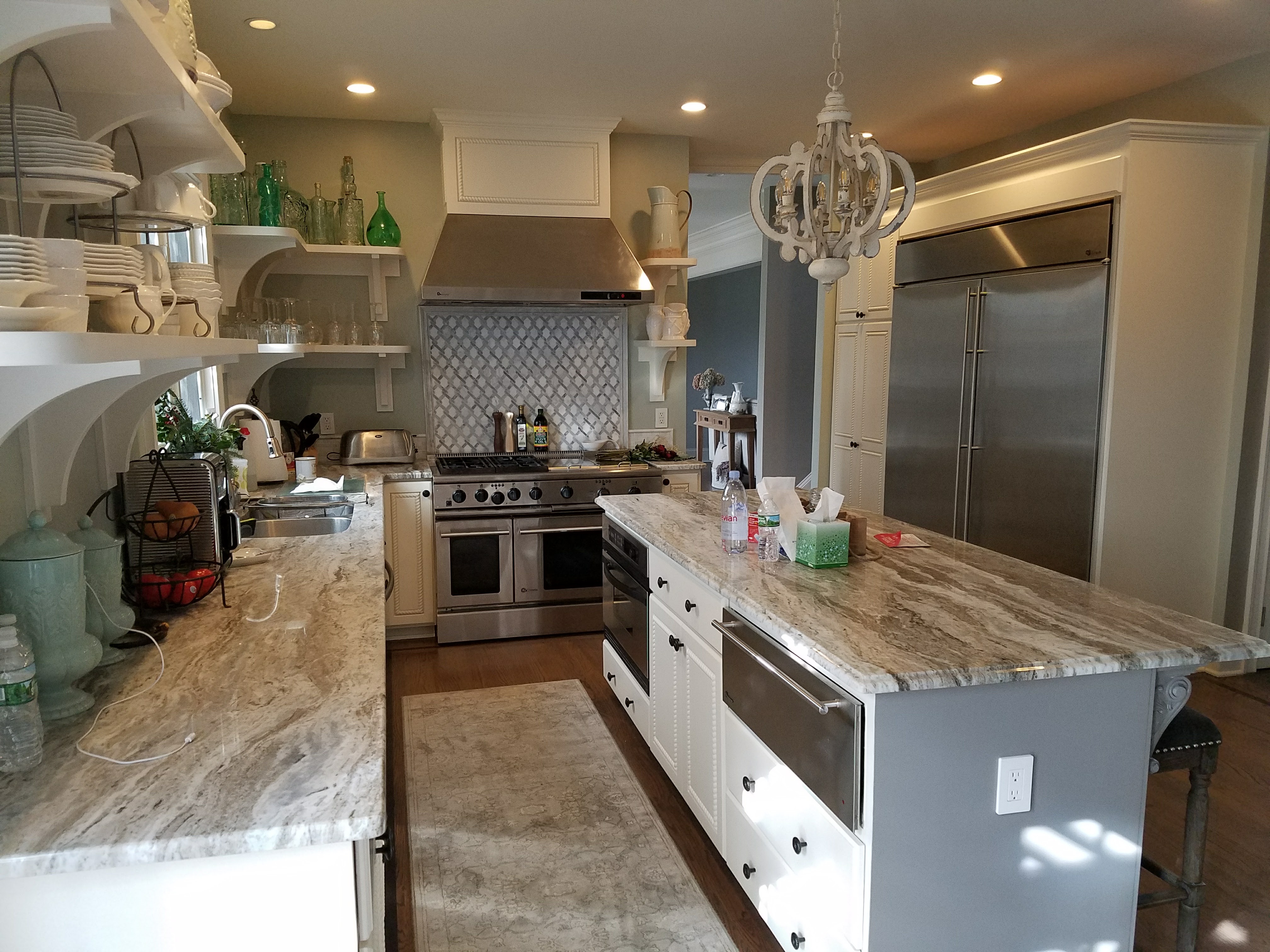 Finished kitchen with granite waterfall countertops, stainless refrigerator, and an ornate chandelier over the island by Rome Leite Home Improvement in Danbury, CT