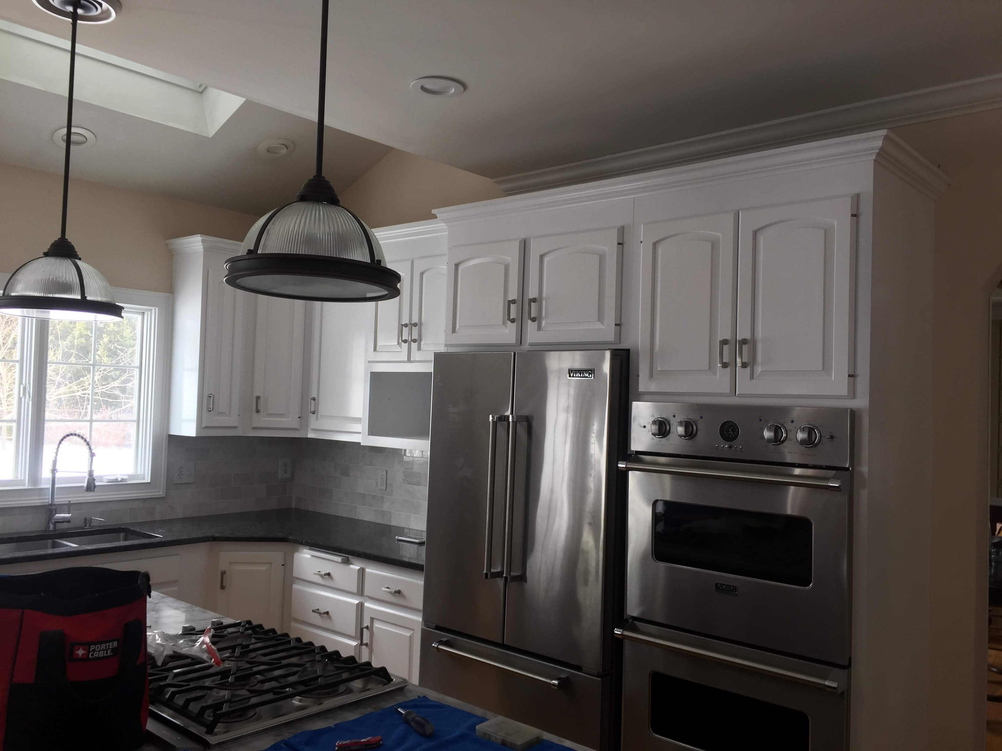 Kitchen with white cabinetry, dark countertops, tile backsplash, and a stainless steel refrigerator and double wall oven by Rome Leite Home Improvement in Danbury, CT