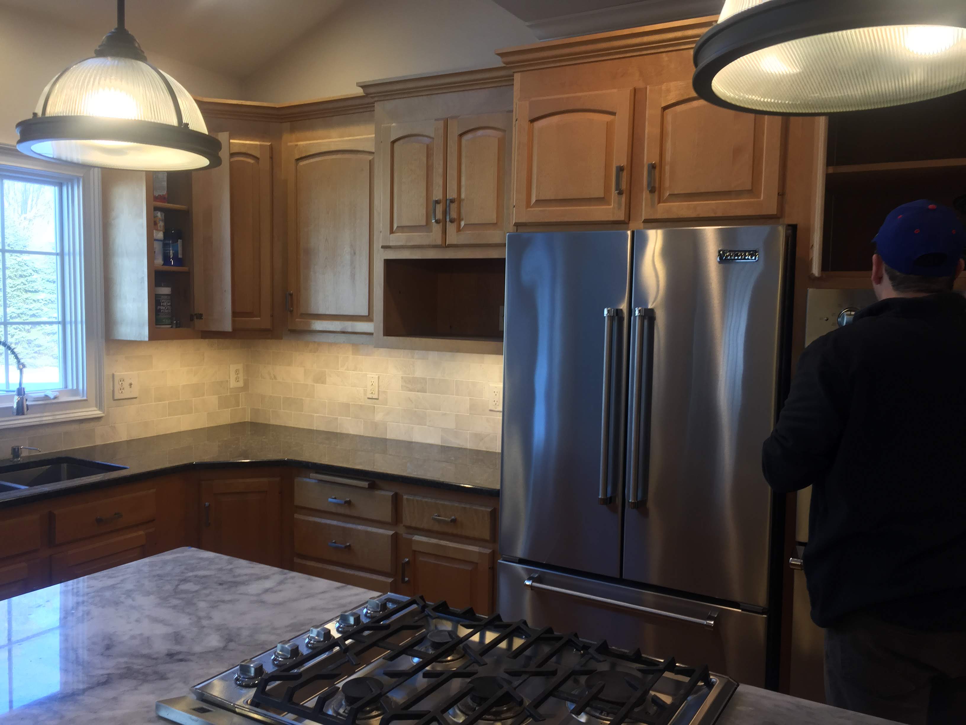 Kitchen with a stainless steel french-door refrigerator, wood cabinets, subway tile backsplash, and pendant lighting by Rome Leite Home Improvement in Danbury, CT